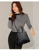 Mulher usando bolsa preta estruturada com alças duplas e transversal, calça preta e blusa xadrez branco e preto