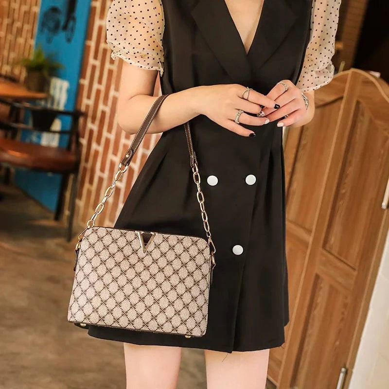 Bolsa Feminina de Couro Elite bege, estampa de monograma, logo "V" dourado. Alça de corrente e transversal. Usada por modelo. Sofisticada e elegante.