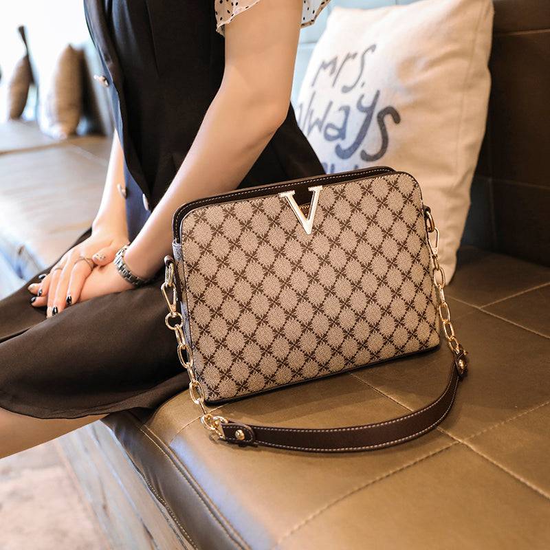 Bolsa Feminina de Couro Elite bege, estampa de monograma, logo "V" dourado. Alça de corrente e transversal. Usada por modelo. Sofisticada e elegante.
