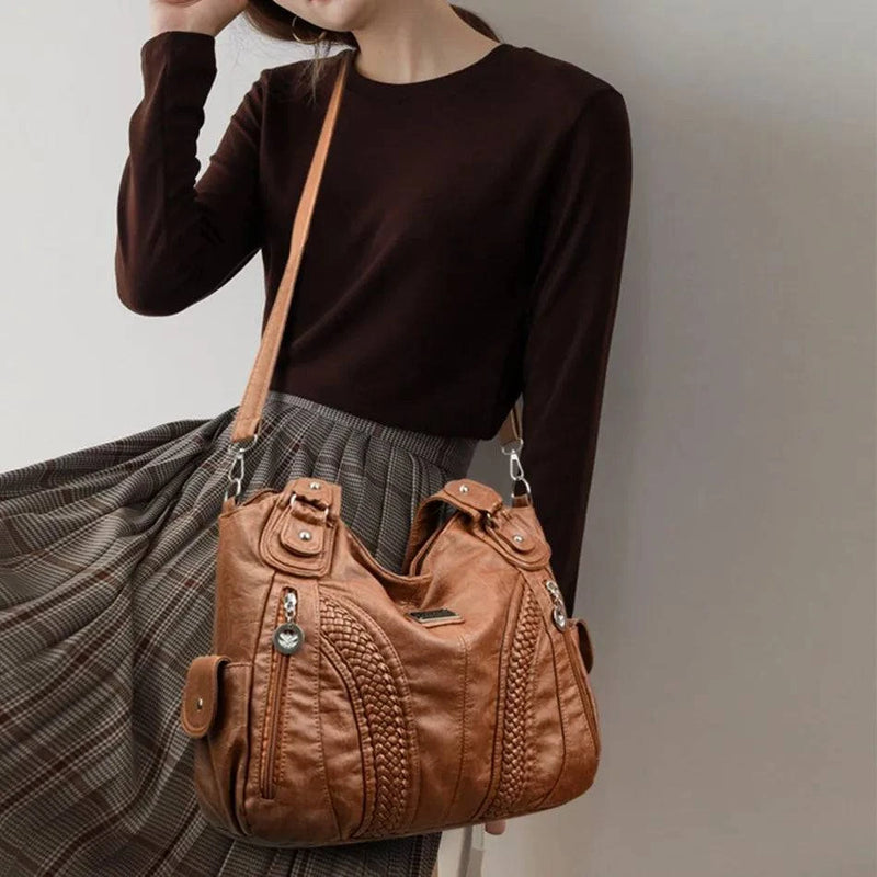 Bolsa feminina de couro legítimo marrom estilo charmosa, com detalhes trançados, alças duplas e alça longa ajustável, combinada com look elegante de blusa preta e saia plissada
