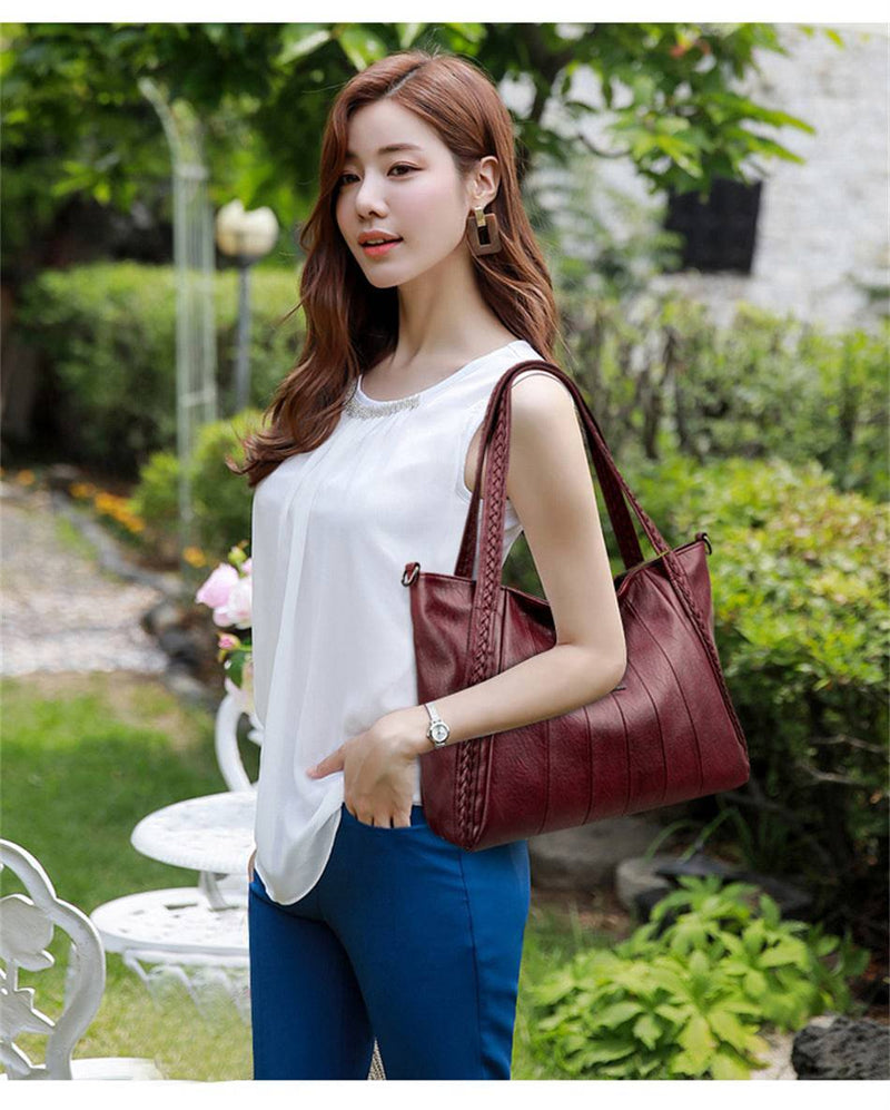 Bolsa Feminina Couro Horizon One vinho. Couro macio com frisos frontais e alças trançadas. Usada por modelo em ambiente externo. Elegante e versátil.