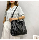 Bolsa preta de couro com alça de ombro, usada com camisa branca e saia plissada