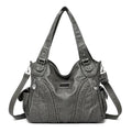 Bolsa feminina de couro legítimo Charmonia na cor cinza, com alças de ombro largas, detalhes trançados na frente, bolsos laterais e zíper prateado.