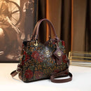 Bolsa de couro marrom com bordado floral vermelho e verde, alças duplas e detalhes metálicos dourados