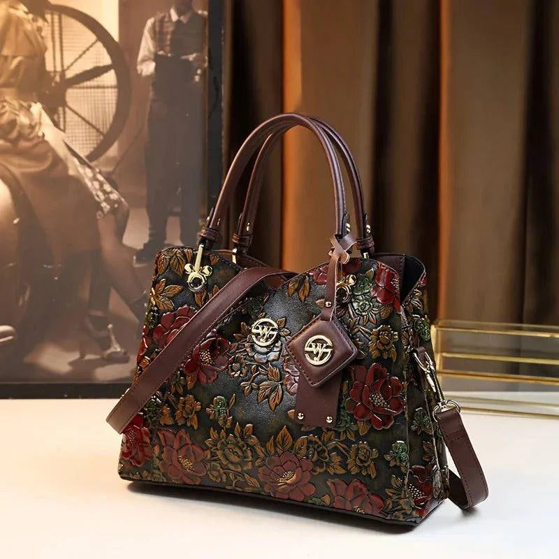 Bolsa Feminina de Couro Puro Luxo, com estampa floral em relevo e tons de vinho, verde e marrom. Alças e detalhes em couro marrom. Estilo vintage e luxuoso.