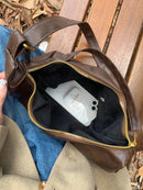 Bolsa Hobo de couro marrom aberta com zíper dourado, mostrando interior forrado e celular dentro