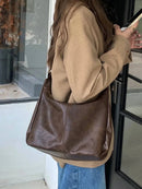 Mulher com bolsa hobo de couro marrom no ombro, alça longa, com cardigan bege