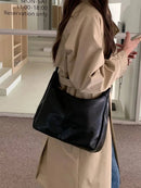 Bolsa feminina de couro Hobo preta, usada no ombro com alça longa, estilo casual, combinada com trench coat bege.
