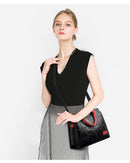 Mulher com blusa preta e saia pregueada cinza carregando bolsa de couro preta com detalhe vermelho
