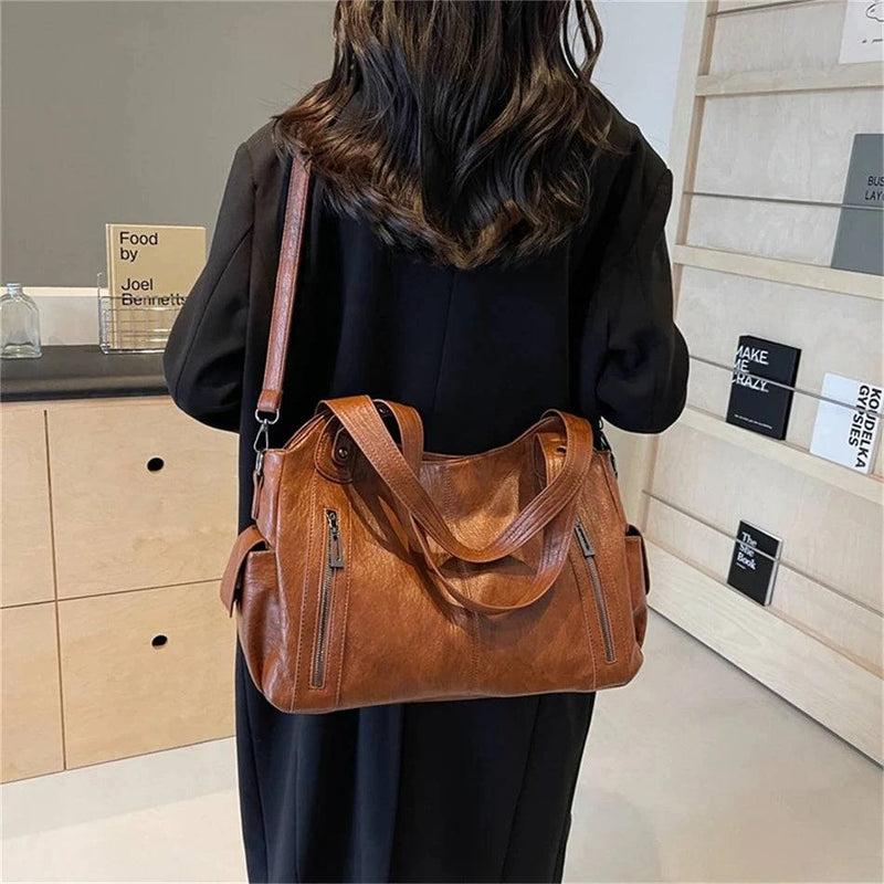 Mulher usando bolsa feminina hobo em couro marrom com alça transversal ajustável e detalhes metálicos em zíper.