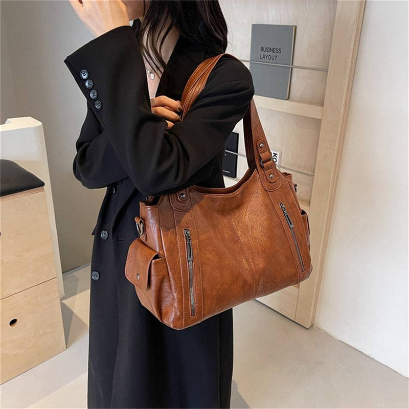 Mulher segurando bolsa feminina hobo em couro marrom com bolsos laterais, zíperes frontais e acabamento sofisticado.