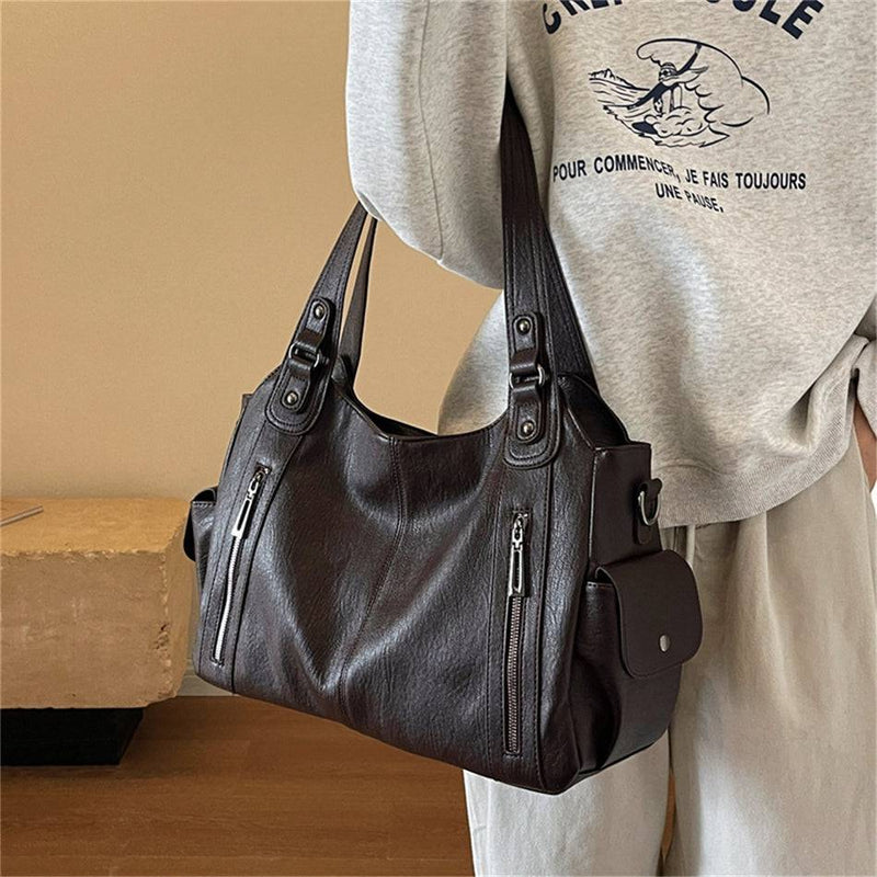 Mulher segurando bolsa feminina hobo em couro marrom escuro com bolsos laterais, zíperes frontais e design moderno.