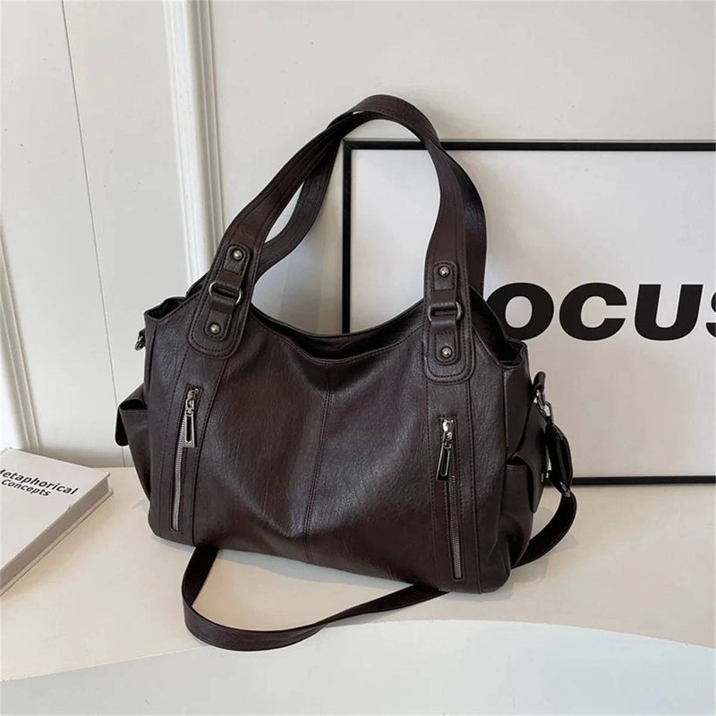 Bolsa feminina hobo em couro marrom escuro com alças reforçadas, zíperes metálicos frontais e bolso lateral.