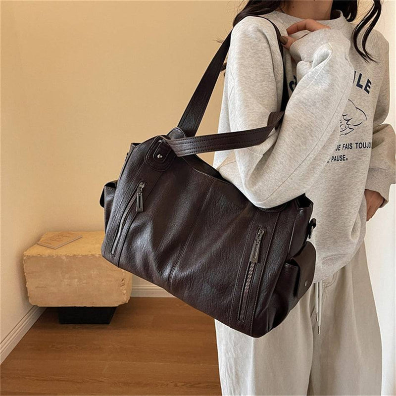 Mulher segurando bolsa feminina hobo em couro marrom escuro, com bolsos laterais e zíperes metálicos, em look casual