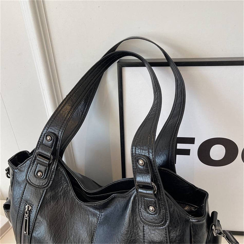 Alças reforçadas da bolsa feminina hobo em couro preto, com detalhes em costura aparente e acabamento metálico.