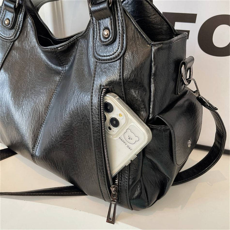 Celular no bolso frontal com zíper da bolsa feminina hobo em couro preto, destacando praticidade e compartimento seguro