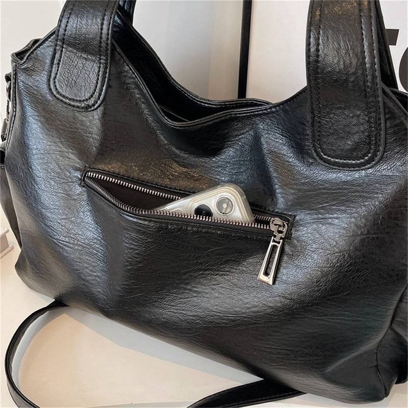 Smartphone dentro do bolso frontal com zíper da bolsa feminina hobo em couro preto, mostrando funcionalidade e espaço interno.