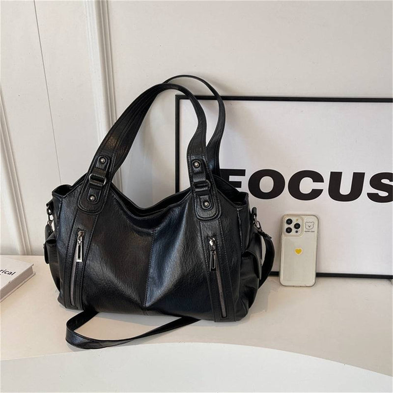 Bolsa feminina hobo em couro preto ao lado de um smartphone, mostrando proporção e tamanho da bolsa.