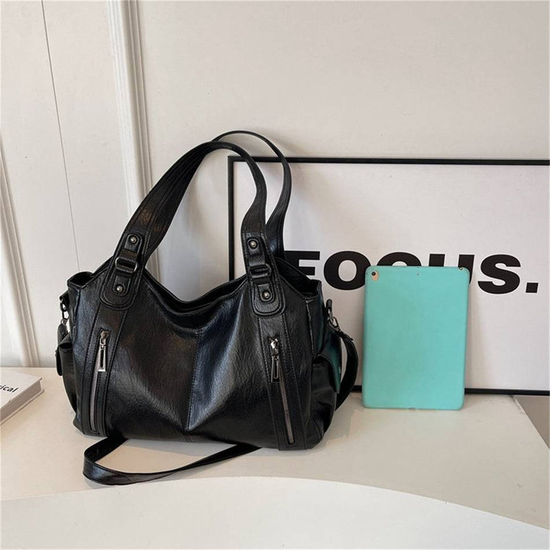 Bolsa feminina hobo em couro preto ao lado de um tablet, mostrando proporção e tamanho do produto.