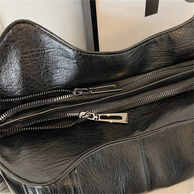 Detalhe do zíper da bolsa feminina hobo em couro preto com acabamento metálico e costura reforçada.