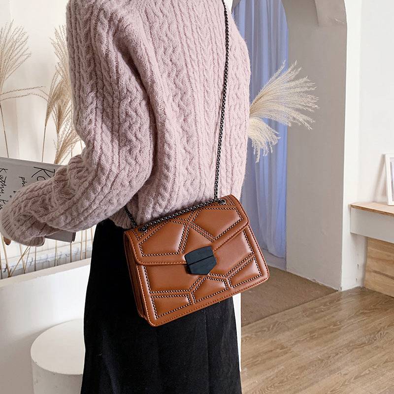 Bolsa Feminina Tiracolo Estruturada na cor caramelo com design matelassê de rebites, fecho frontal geométrico e alça de corrente escura, ideal para um visual moderno e versátil.