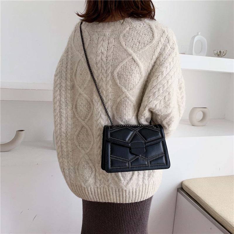 Bolsa Feminina Tiracolo Estruturada preta com design matelassê de rebites e alça de corrente escura, sendo usada nas costas, mostrando o caimento perfeito e o estilo da peça.