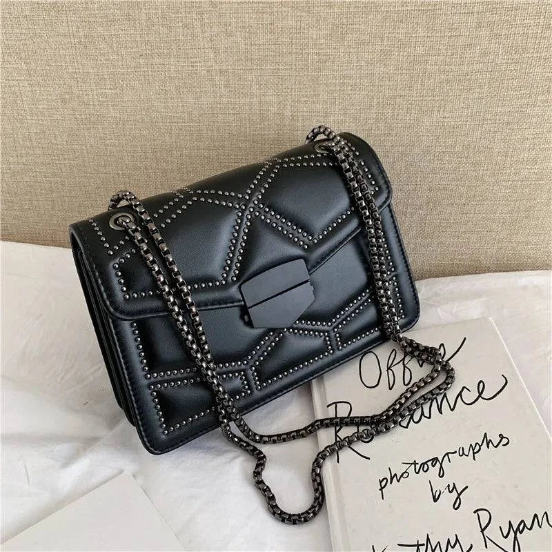 Bolsa Feminina Tiracolo Estruturada preta com detalhe matelassê de rebites, fecho frontal diferenciado e alça de corrente escura, perfeita para um look moderno e urbano.