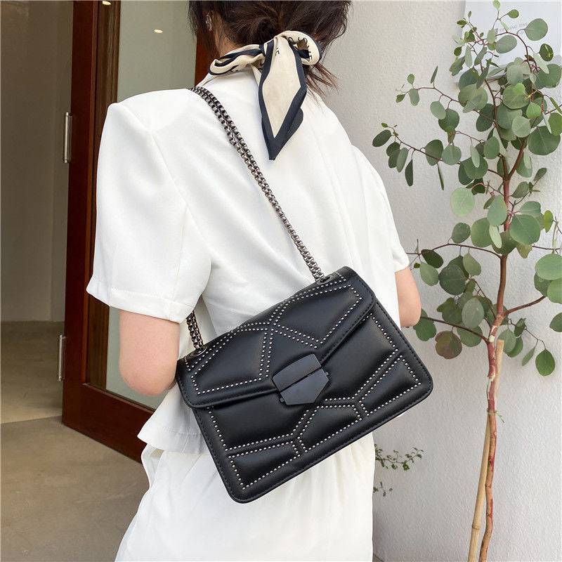 Bolsa Feminina Tiracolo Estruturada preta com design matelassê de rebites e alça de corrente escura, exibida nas costas, destacando seu caimento e estilo moderno.
