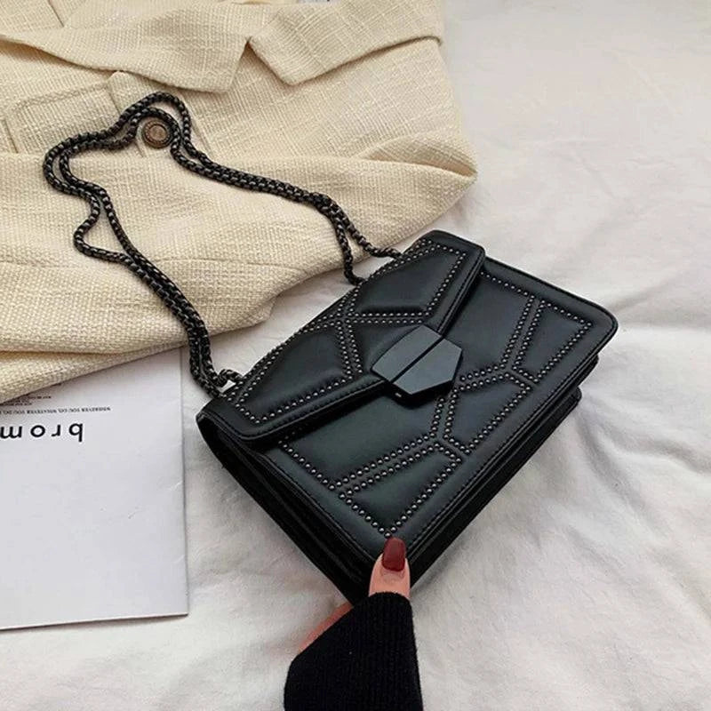 Bolsa Feminina Tiracolo Estruturada preta com design matelassê de rebites em formato geométrico, fecho frontal moderno e alça de corrente escura, ideal para complementar diversos looks.