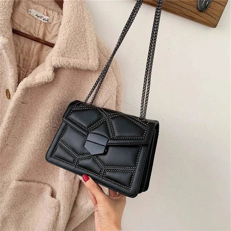 Bolsa Feminina Tiracolo Estruturada preta com detalhes em rebites e design geométrico, fecho moderno e alça de corrente escura, perfeita para adicionar um toque de estilo e atitude ao seu visual.
