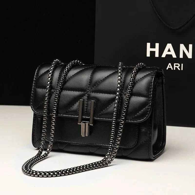 Bolsa Feminina Tiracolo Matelassê preta, design acolchoado elegante, alça de corrente metálica e fecho de metal distintivo.