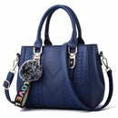 Bolsa tote estruturada azul-marinho com textura chevron, alças duplas e chaveiro pompom cinza