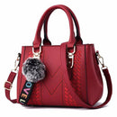 Bolsa tote estruturada vermelha vinho com textura chevron, alça transversal e pompom cinzento