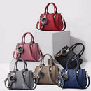 Coleção de bolsas tote médias estruturadas de couro Giovanna em diversas cores (vermelho, rosa, preto, taupe, marrom, azul), todas com alça transversal e chaveiro de pompom com "LOVE".
