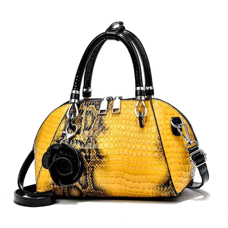 Bolsa de Mão Monarca amarela e preta, textura de cobra. Design semiesférico, alças pretas, ferragens prateadas. Charm de rosa preta. Elegante e sofisticada.