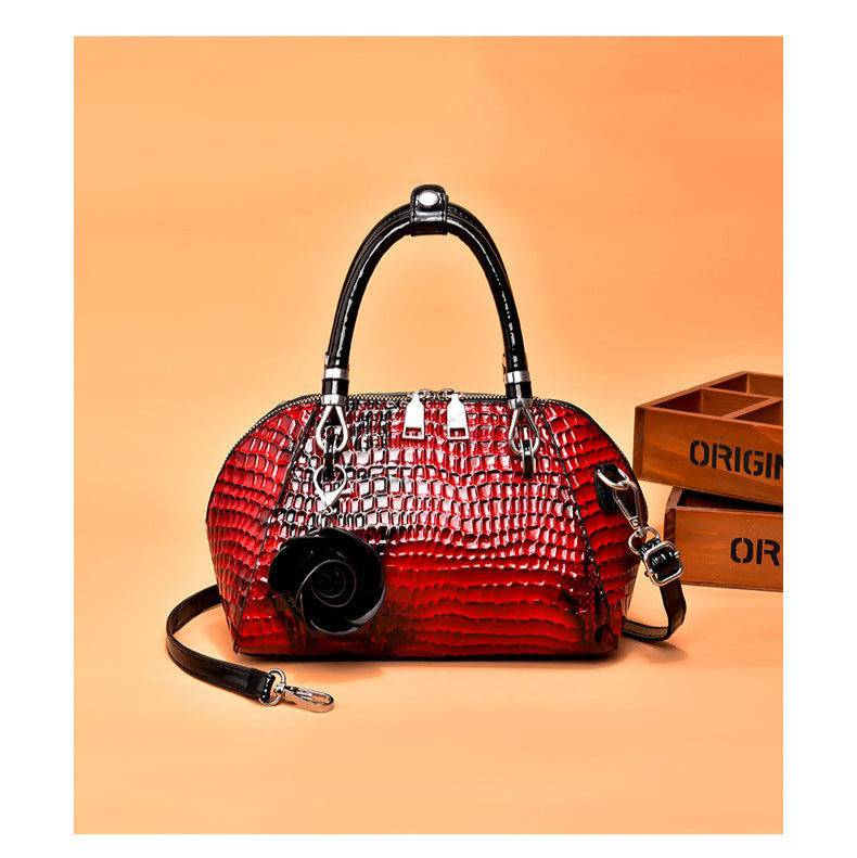 Bolsa de Mão Monarca vermelha, couro com textura croco brilhante. Design semiesférico, alças pretas, charm de rosa. Elegante e sofisticada.