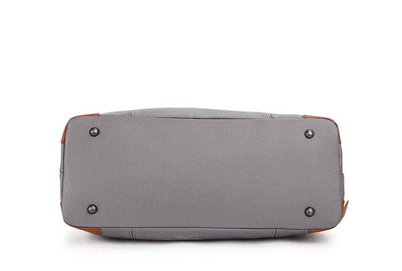 Detalhe da base da bolsa de ombro feminina em couro legítimo cinza, com reforço nas laterais e pés metálicos de apoio.