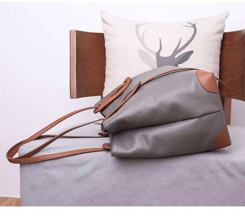 Detalhe da base lateral da bolsa de ombro feminina em couro legítimo cinza com cantos reforçados em marrom, alças finas longas.