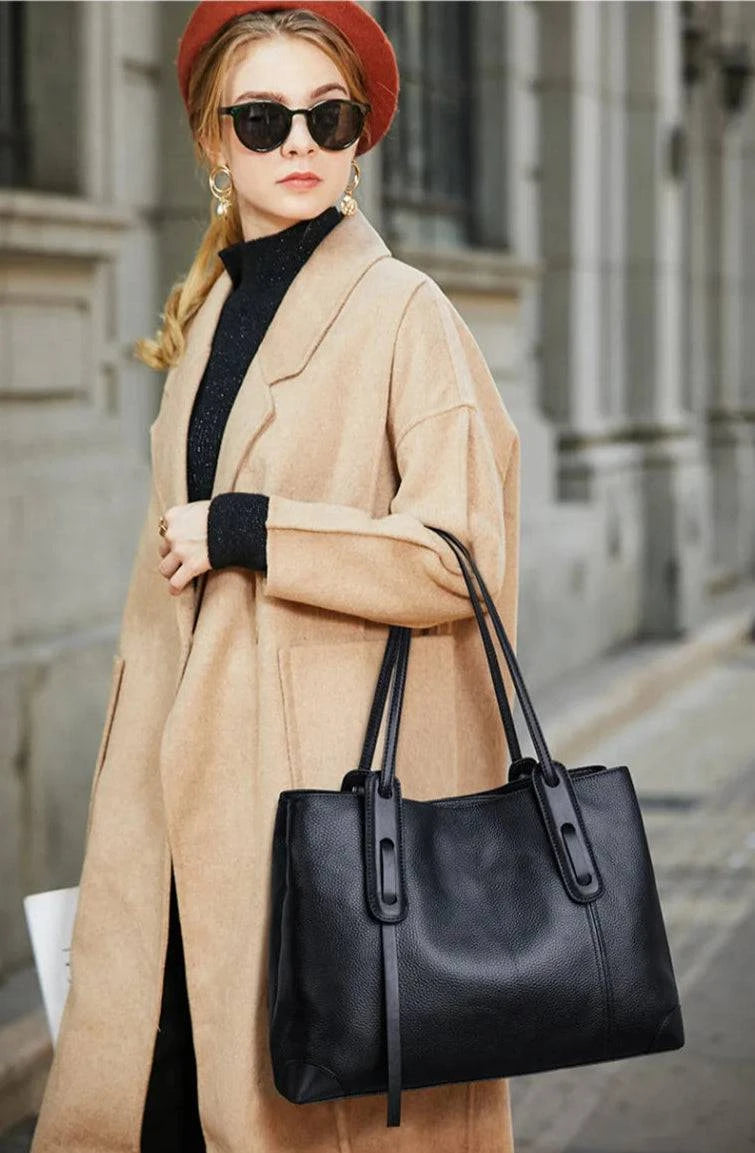 Mulher usando bolsa de ombro feminina em couro legítimo cinza com alças marrons, em look executivo com blazer claro.