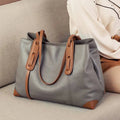 Bolsa de ombro feminina em couro legítimo, na cor cinza com detalhes e alças marrons, design elegante sobre sofá bege.
