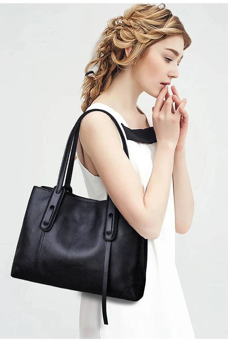 Mulher segurando bolsa de ombro feminina em couro legítimo preto, com alças elegantes e acabamento texturizado, em look sofisticado.