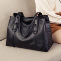 Bolsa de ombro feminina em couro legítimo preto, com textura elegante e design sofisticado, sobre sofá bege.