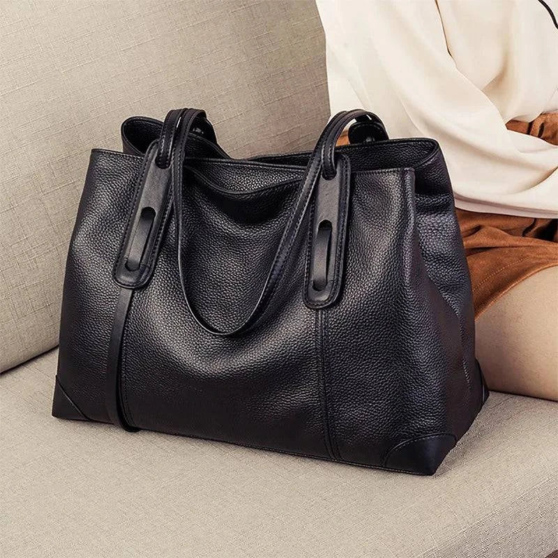 Bolsa de ombro feminina em couro legítimo preto, com textura elegante e design sofisticado, sobre sofá bege.