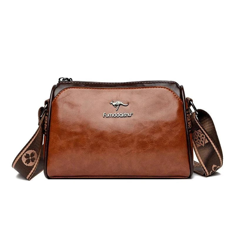 Shoulder Bag Bolsa Feminina de Couro marrom-caramelo. Design de dois tons, logo metálico de canguru e alça estampada larga. Elegante e versátil.