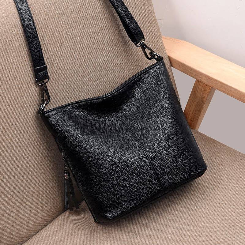Bolsa tiracolo de couro feminina Ladies preta com textura granulada e alça transversal ajustável, exibida sobre uma cadeira em ambiente de estúdio, destacando seu design macio.
