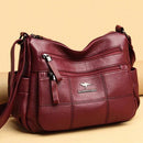 Bolsa tiracolo de couro feminina vinho com textura granulada e painéis em matelassê, múltiplos bolsos frontais com zíper e logotipo de canguru em relevo.