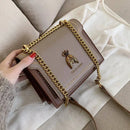 Bolsa tiracolo feminina de couro estruturada em bege e marrom, com alça de corrente dourada e fecho decorativo em forma de abelha.