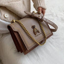 Bolsa tiracolo feminina de couro estruturada na cor bege com detalhe em corrente dourada e aplicação decorativa de abelha no fecho.