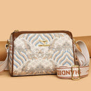 Bolsa tiracolo feminina com padrão ondulado azul e dourado, alça em couro marrom e logo dourado.