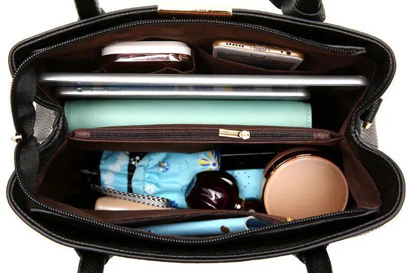 Visão superior do interior aberto da bolsa tote Eliza preta, revelando ampla capacidade para tablet, celular, cosméticos e outros pertences essenciais, com forro escuro.
